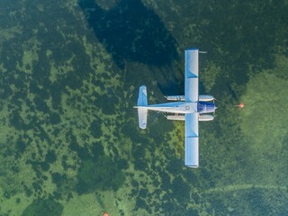 Aerial view of a seaplane anchored in shallow, clear water. The pilot is preparing for takeoff,...