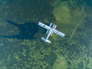 Aerial view of a seaplane, a single-engine aircraft with floats, parked in shallow water near buoys. The plane is stationary, possibly for maintenance or a break. USA.