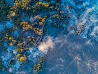 Aerial view of Wai-O-Tapu geothermal area in New Zealand. A wooden walkway allows tourists to safely explore the hot springs and bubbling mud pools. Steam rises from the geothermal landscape.