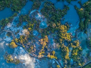 Aerial view of Wai-O-Tapu geothermal area in New Zealand. A wooden boardwalk allows tourists to safely view the hot springs and bubbling mud pools. Steam rises from the geothermal activity.