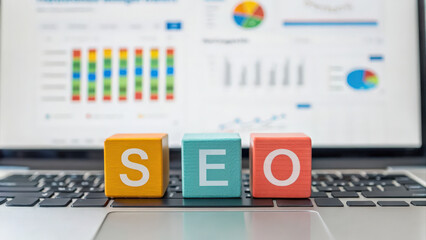 Colorful SEO blocks on a laptop with graphs and charts in the background, highlighting digital marketing analytics and performance metrics.