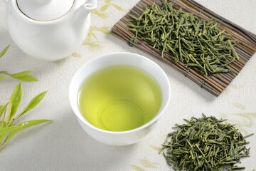 Photo of Green tea in a white cup, a white teapot and dried green tea leaves are placed beside it , Generative AI