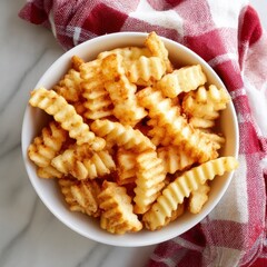 Overhead view of crinkle cut fries in a white bowl with red and white checkered cloth on marble
