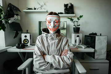 Stylish individual in cyber mask sits at gaming setup, surrounded by tech gear and modern decor,...