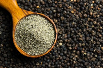 Black pepper powder in wooden cup spoon with black peppercorns background. Food ingredients. Aromatic spice. Top view