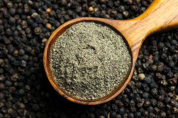 Black pepper powder in wooden cup spoon with black peppercorns background. Food ingredients. Aromatic spice. Top view