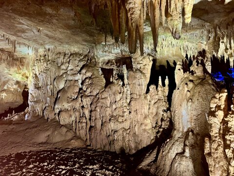 Stalactites and stalagmites emerge from the damp cave walls, illuminated by soft lighting. The atmosphere is cool and mysterious, inviting exploration beneath the surface