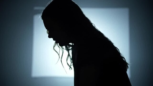 Silhouette of woman head bowed against luminous rectangle