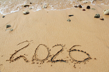 New Year 2026, inscription on the beach with sea wave. Number 2026 on the seashore, handwritten message on the sand. New Year concept.