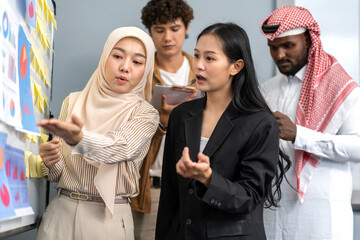 Diverse team analyzing charts and sticky notes on whiteboard during business meeting, arab, asian and muslim coworkers discussing data insights, teamwork, corporate strategy, startup planning session