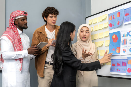 Diverse team analyzing charts and sticky notes on whiteboard during business meeting, arab, asian and muslim coworkers discussing data insights, teamwork, corporate strategy, startup planning session