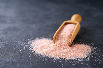 himalayan salt in a small wooden shovel on a black kitchen table, selective focus.
