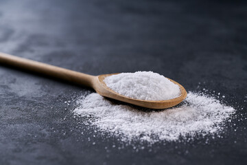 salt in a wooden spoon on a black stone table, selective focus.