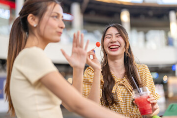 Happy asian friends enjoying summer moment laughing and sharing watermelon smoothie outdoors, fun travel vibes, healthy lifestyle and playful chill out experience in vibrant urban setting