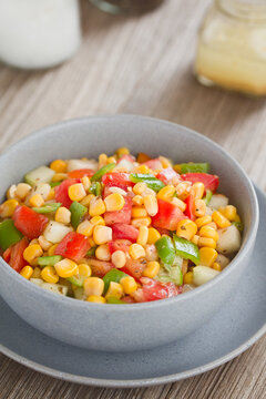 Colorful vegetable salad made of tomato, green pepper, cucumber and corn kernels, served in bowl, with vinaigrette in the back (Selective Focus, Focus in the middle of the image) 