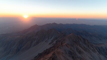 Aerial shot of mountain range at sunrise with sun rising over peaks, orange sky