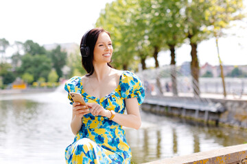Happy woman listening music in a park with headphones a sunny day near lake
