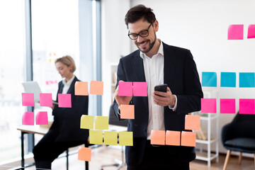 Business individuals, man and woman, collaborating on project using colorful notes on glass board....
