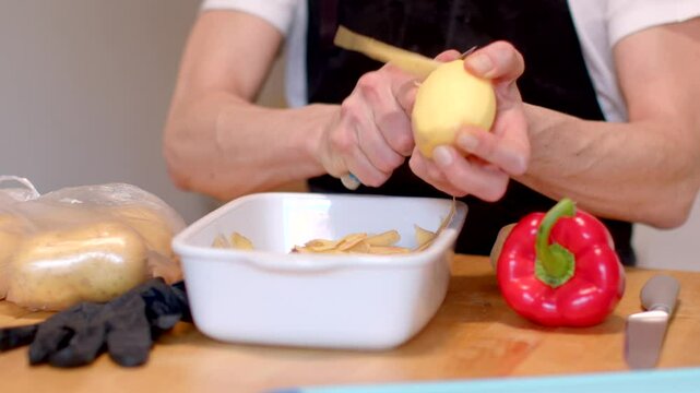 A person peels potatoes on a kitchen countertop with a bright red bell pepper beside them