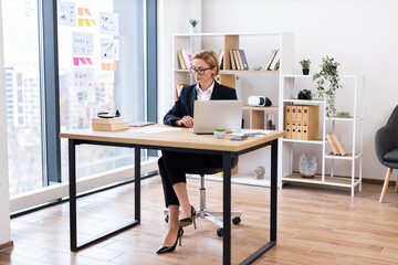 Middle-aged Caucasian woman working on laptop in bright modern office setting, symbolizing...