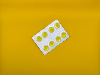 Yellow tablets in silver packaging on yellow background in the center of the image, top view