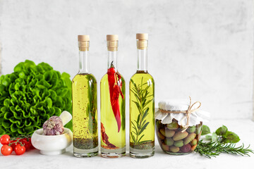 Different types of olive oil with rosemary, thyme and red pepper on a white background.