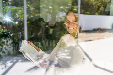 Young woman smiling by the window reading a book