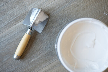 The spatula for the corners and the jar with putty. Laminated grey background. Repair concept, repair goods stores. Top down view. Copyspace