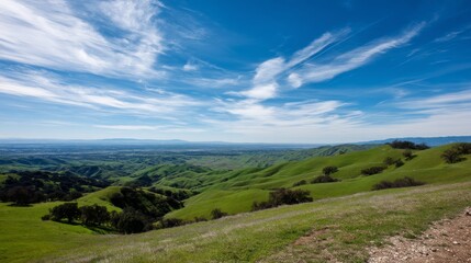 Fototapeta premium Explore a tranquil mountain valley blanketed in lush green hills, gently illuminated by sunlight and featuring a clear blue sky with wispy clouds, inviting calmness