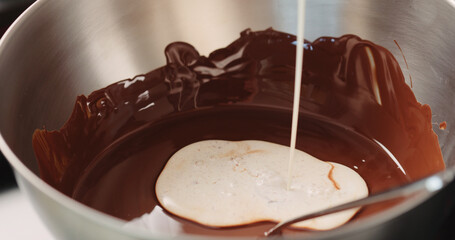 adding cream into melted chocolate in steel bowl