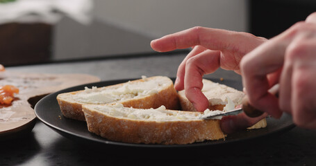 man spread cream cheese on ciabatta slice on black plate
