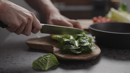 man hand cutting romaine lettuce on wood board to make salad