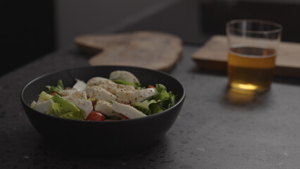 salad with mozzarella and tomatoes in black bowl and apple cider in glass on concrete countertop