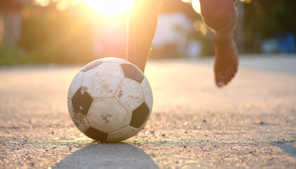 child playing soccer with worn ball on sunny day, capturing joy and energy of outdoor play. sunlight creates warm atmosphere, enhancing playful moment