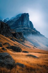 Misty Cliffside Mountain Rising Above Golden Grass Hillside in Autumn Light, Dramatic Landscape with Steep Rocky Slopes, Rugged Nature Scene Evoking Solitude, Wilderness, and Majestic Elevation