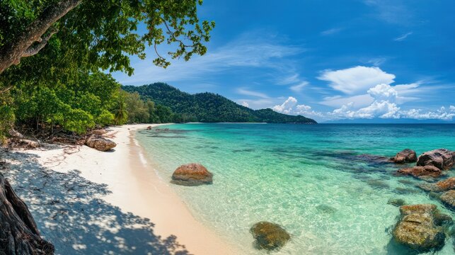 Tranquil tropical beach with clear turquoise waters soft white sand rocky shoreline lush green foliage under bright blue sky with scattered clouds scenic natural coastline paradise