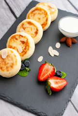 Delicious sweet cottage cheese pancakes served with fresh strawberries and cream on a black stone for breakfast