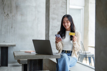Happy freelancer is making an online payment using credit card and smartphone while sitting at a...