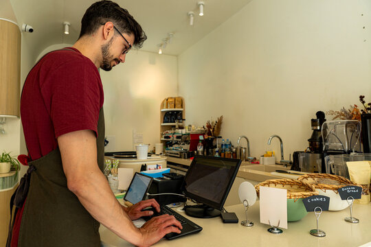 Barista working at the counter of a modern coffee shop, using a point of sale system to manage orders