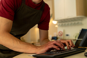 Barista wearing an apron, typing on a keyboard while processing customer orders in a bustling coffee shop environment