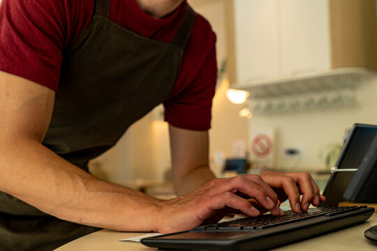 Barista wearing an apron, typing on a keyboard while processing customer orders in a bustling coffee shop environment