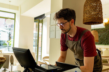 Young cashier working diligently at the cash register in a bustling restaurant, managing orders and...