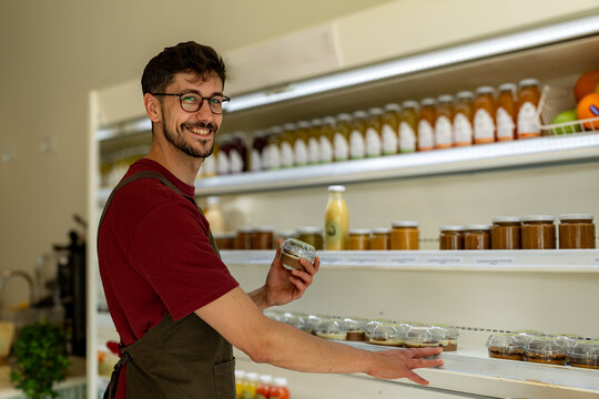 Smiling shopkeeper arranging food products on shelves, creating an inviting display in a small grocery store filled with fresh, organic items