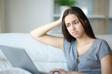 Confused woman checking laptop content in a house