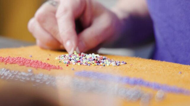 Macro shot revealing an old Metis women's hands as she one by one puts beads through a needle to prepare for making handcrafted Indigenous crafts. The craft takes technique and patience.