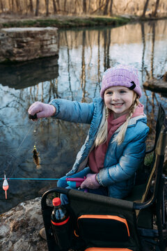 Young child holds up fish caught on riverbank