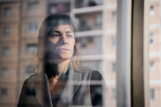 Thoughtful woman looking out of a window with a cityscape reflection