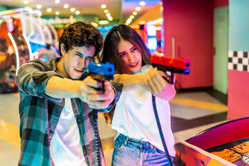 Young couple playing arcade shooting game together in amusement park