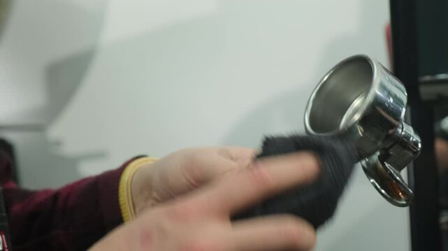Male barista holds component of coffee machine wiping with cloth. Cleaning portafilter after coffee to maintain cleanliness of equipment slow motion