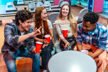 Cheerful multiethnic friends enjoying bowling alley games and drinks
